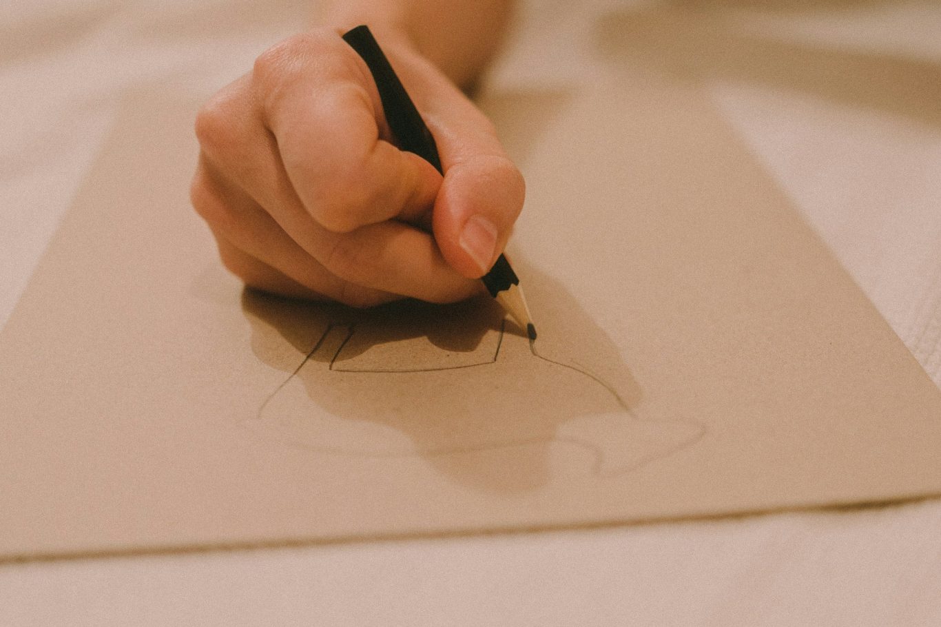 Eine Hand zeichnet mit einem Stift auf braunem Papier. Eine Hand zeichnet mit einem Stift auf braunem Papier.