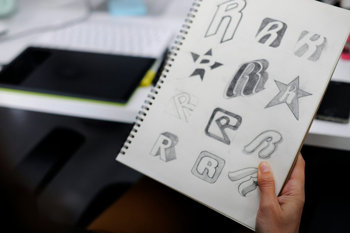 Eine Hand hält ein Skizzenbuch mit verschiedenen Buchstaben und Sternen in unterschiedlichen Designs. Eine Hand hält ein Skizzenbuch mit verschiedenen Buchstaben und Sternen in unterschiedlichen Designs.